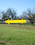 Yellow rubber gate handle for electric fence on a wire with a blurred background of trees and sky