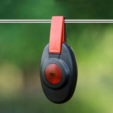 Black and red Patriot fence alert clip-on fence light hanging on a wire with a green blurred background
