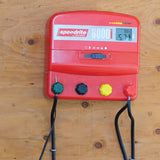 Red speedrite electric fence charger mounted  on a wooden barn surface