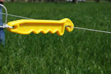 Yellow Electric Fence gate handle at farm with green pasture on poliwire
